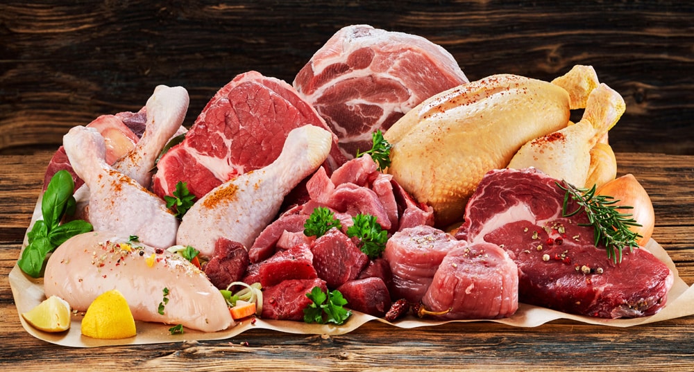 Raw meat assortment, beef, chicken, turkey, decorated with greens and vegetables, placed on cooking paper on wooden table